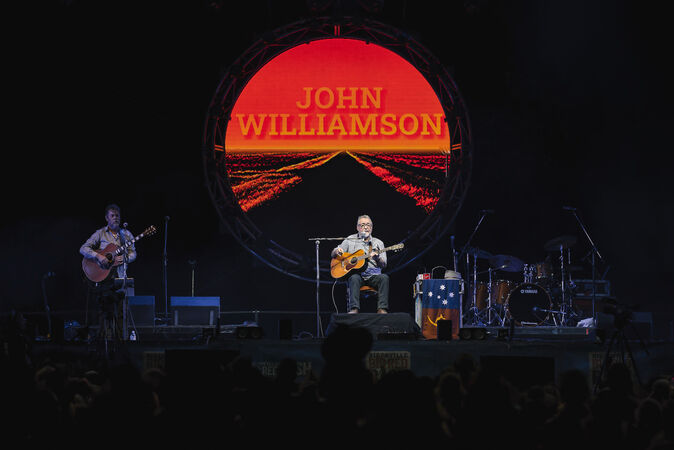 Singer on concert stage sitting on chair and holding guitar