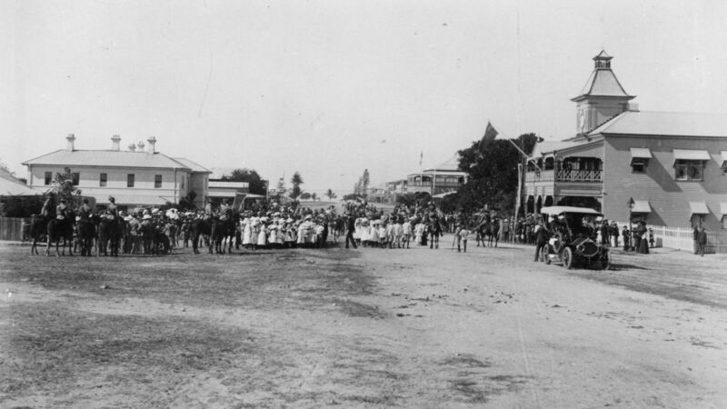 Crowd gathered on early 1900s dirt street with motor car