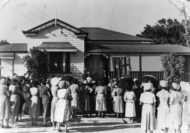 Women gathered outside Queenslander house with Australian flag hanging on verandah