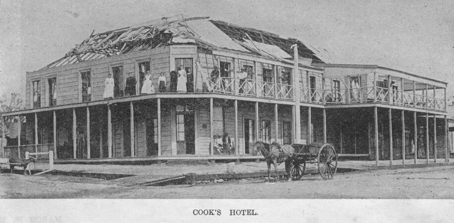 People standing on ruined verandah of unroofed building with horse and cart on street