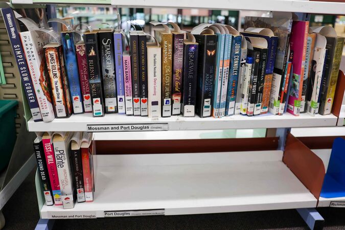 Library books on shelves labelled Mossman and Port Douglas