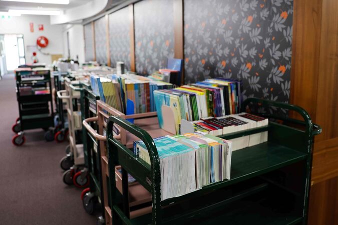 Trolleys of books against a flowered wallpapered wall