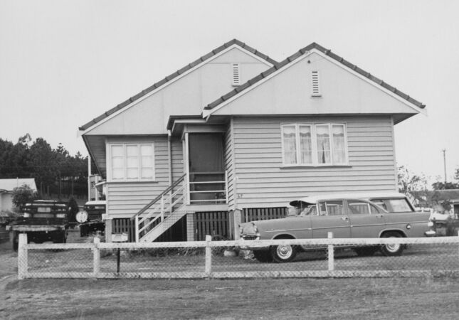 Black and white of single-storey house on stumps with car parked out front