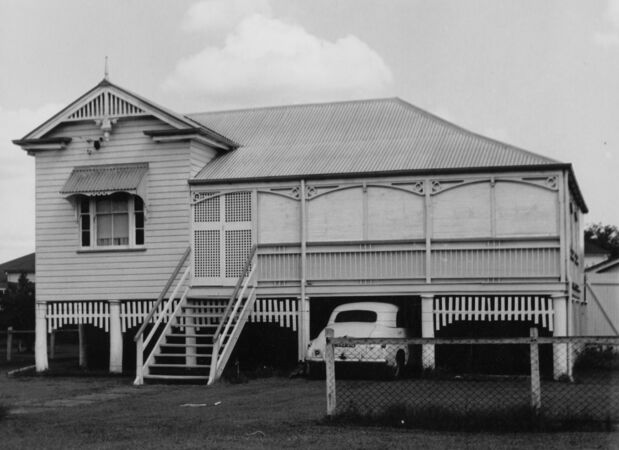 Black and white of Queenslander on stympes with enclosed front verandah and vintage car parked underneath