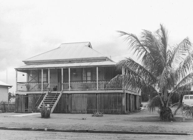Queenslander house in black and white with large palm tree at right