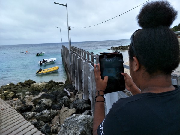 A woman uses an iPad to take a picture of a jetty and boats