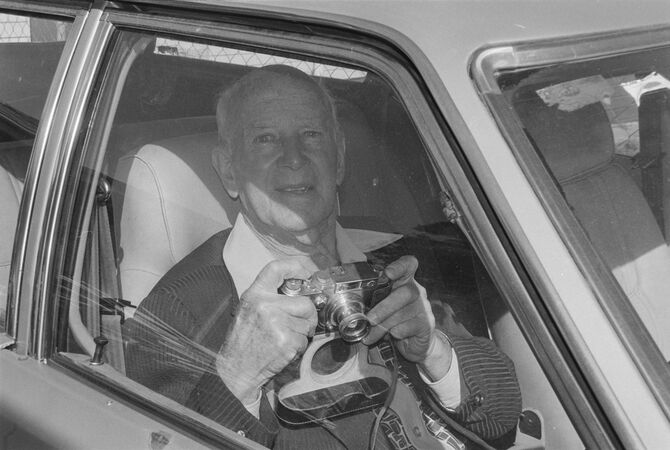 Elderly man sitting in driver's seat of car holding old film camera