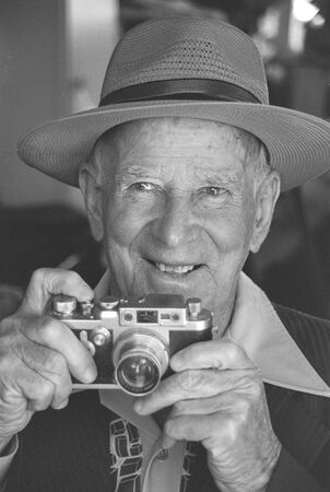 Man in panama hat holding 35mm film camera near face