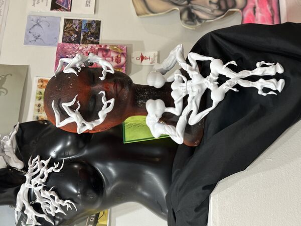 A close up photo of a black and white head bust, that is covered in white 3d models. One is a long piece along the neck of the bust and hangs down like a necklace and then two other pieces fit around the eyes of the head.