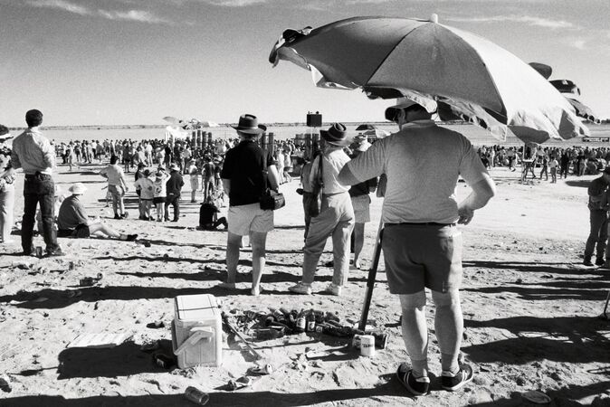 Man standing under beach umbrella in crowd watching horses races