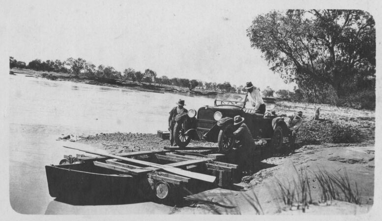 men guiding 1920s car onto to small boat at riverbank