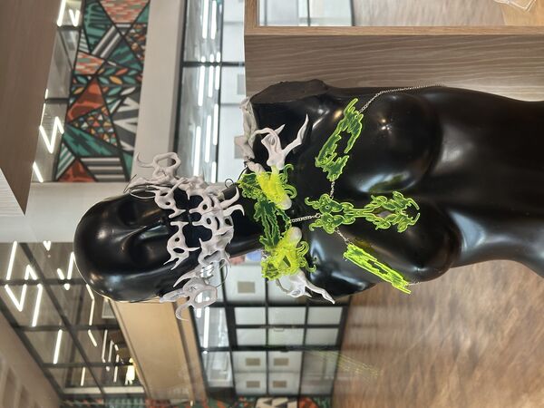 A close up photo of a black mankin that cuts of under the torso. The the chest of the manakin is a neon green laser cut Wearable Sculpture. Around the shoulders is a 3D modelled white Wearable Sculpture and the face of the manakin is covered by a white modelled 3D Wearable Sculptures that appears like a mask.