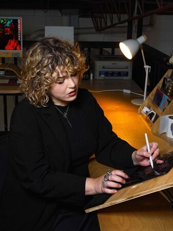 Curly-haired woman drawing on iPad at desk using stylus