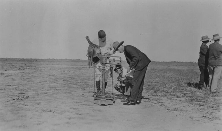 Jockey with saddle being weighed at outback races with two officials checking weight