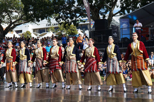 Women dressed in traditional Greek clothing preforming a dance on stage.