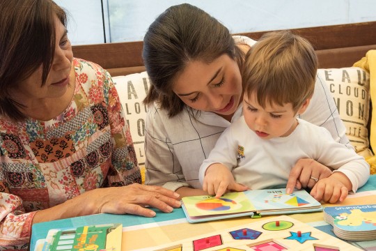 Child learning with two women through reading a book.