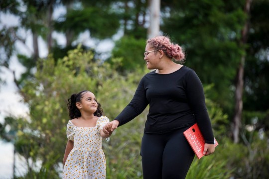 Mother and daughter walking outside holding hands. Mother is holding a book titled Koalas Like To ... written by Written by Shae Millward.