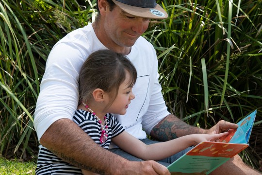 Man reading a book to a girl in an outside area