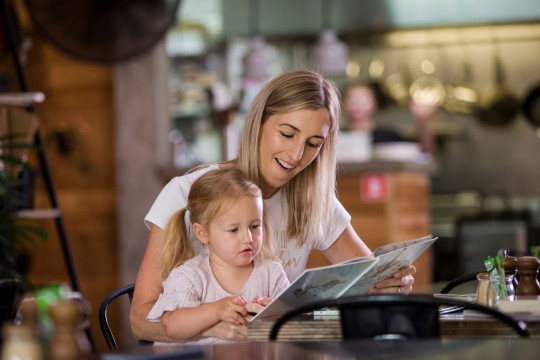 Woman and girl share a book at a table 