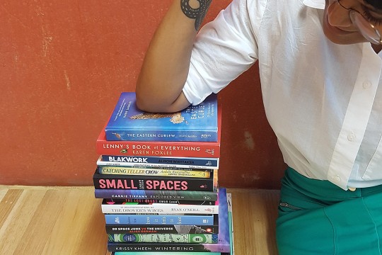 Shastra Deo sitting on a wood floor leaning her elbow against a stack of books