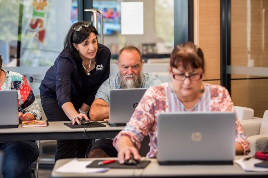 An instructor helps a group of people using laptops in a classroom.