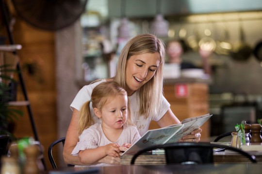 Woman and a girl share a book at a cafe.