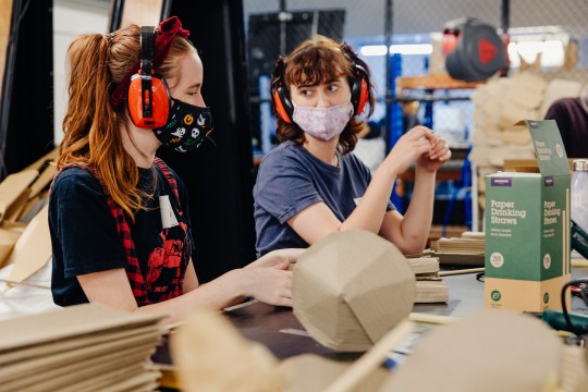 2 young females with masks and earmuffs in a fabrication lab