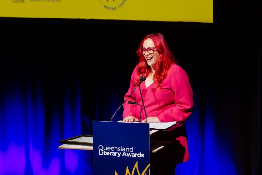 Melanie Saward at the 2023 Queensland Literary Awards. She stands onstage at a lectern reading from a speech.