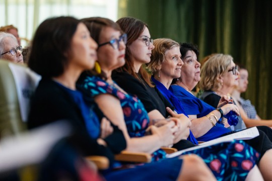 People sitting in a row in an auditorium. 