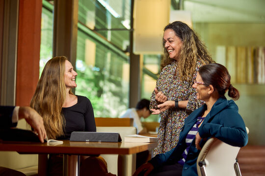 Three visitors talking and smiling together at a table at State Library.