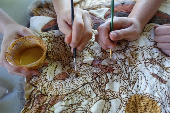 Two artists painting a possum skin cloak with ochre