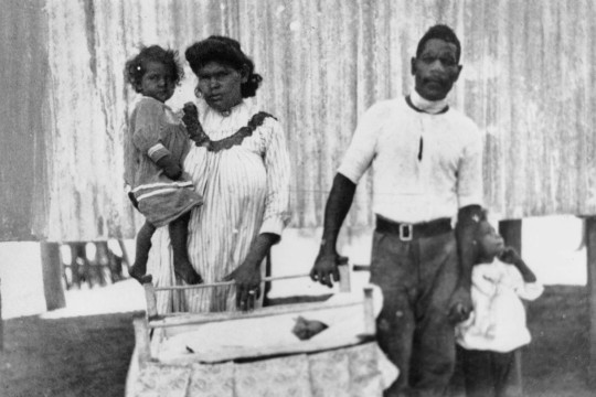 Two Aboriginal parents and their two children standing behind a babys cot
