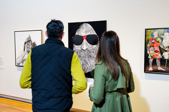 Two people looking at a wall of paintings.