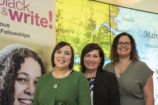 Three Indigenous women smiling in front of an artwork