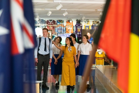 Teacher with high school students in kuril dhagun, the State Library First Nations space. There are the Australian and Aboriginal flags in the foreground.