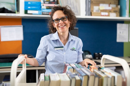 Smiling librarian from Moreton Bay Region Library holding onto a book trolley
