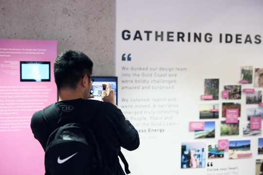 Man taking photo on a smart phone in State Library's Bright Bold Boundless: Designing the Queen's Baton display.