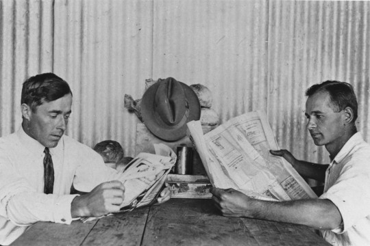 Two men sitting at a table reading newspapers ca. 1929