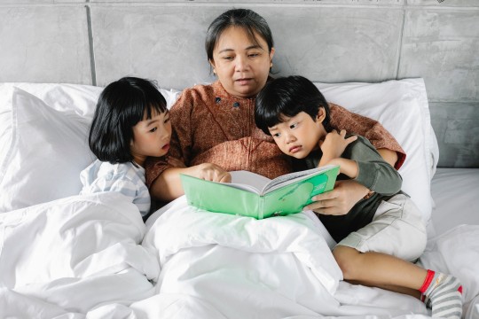 Lady reading a book with 2 children in bed