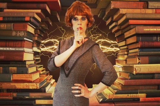 A woman dressed comically as a librarian shushing with her finger in front of her lips set against a background of books