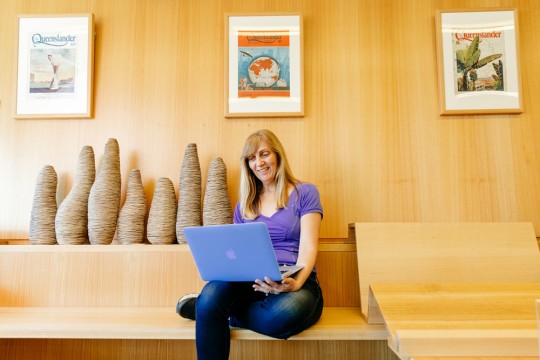 Woman sitting at the library with a laptop on her lap.