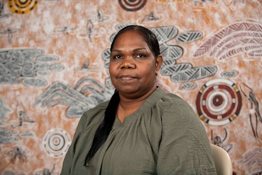 Portrait of Colleen Sam in front of her artwork Ngundurra Dreaming, 2025, photo by State Library of Queensland.