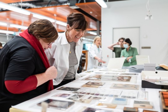 Two women looking at old photos and documents displayed on a title.