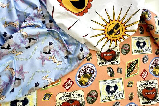 A collection of three different vibrant prints are in a flat lay, one in peach hues, one in purple and one with bright sun designs on a white background