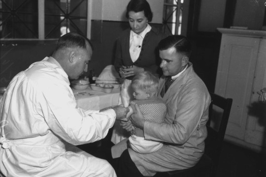 A black and white photograph of Dr Weaver immunising a child while a nurse looks on Brisbane 1941