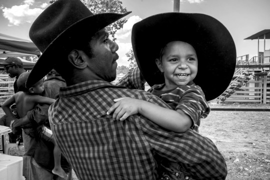 Man in a wide brimmed hat holding a smiling child wearing a wide brimmed hat.