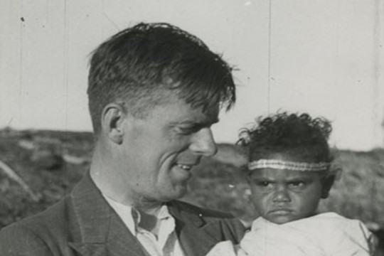 Black and white image of Dr Norman Tindale holding a young Aboriginal child