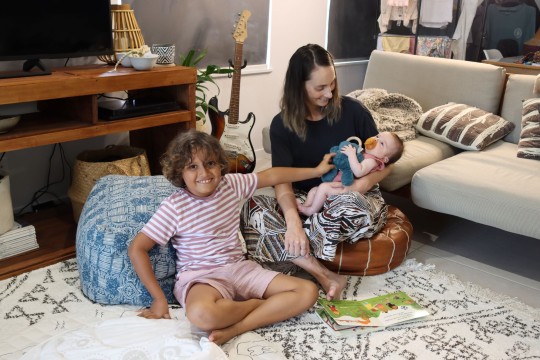 Mother with baby and child sitting on floor reading a book