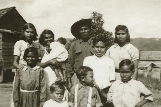 First Nations family outside wood building.