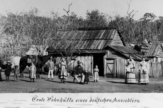 11 people of various ages standing in front of a wooden house and a horse